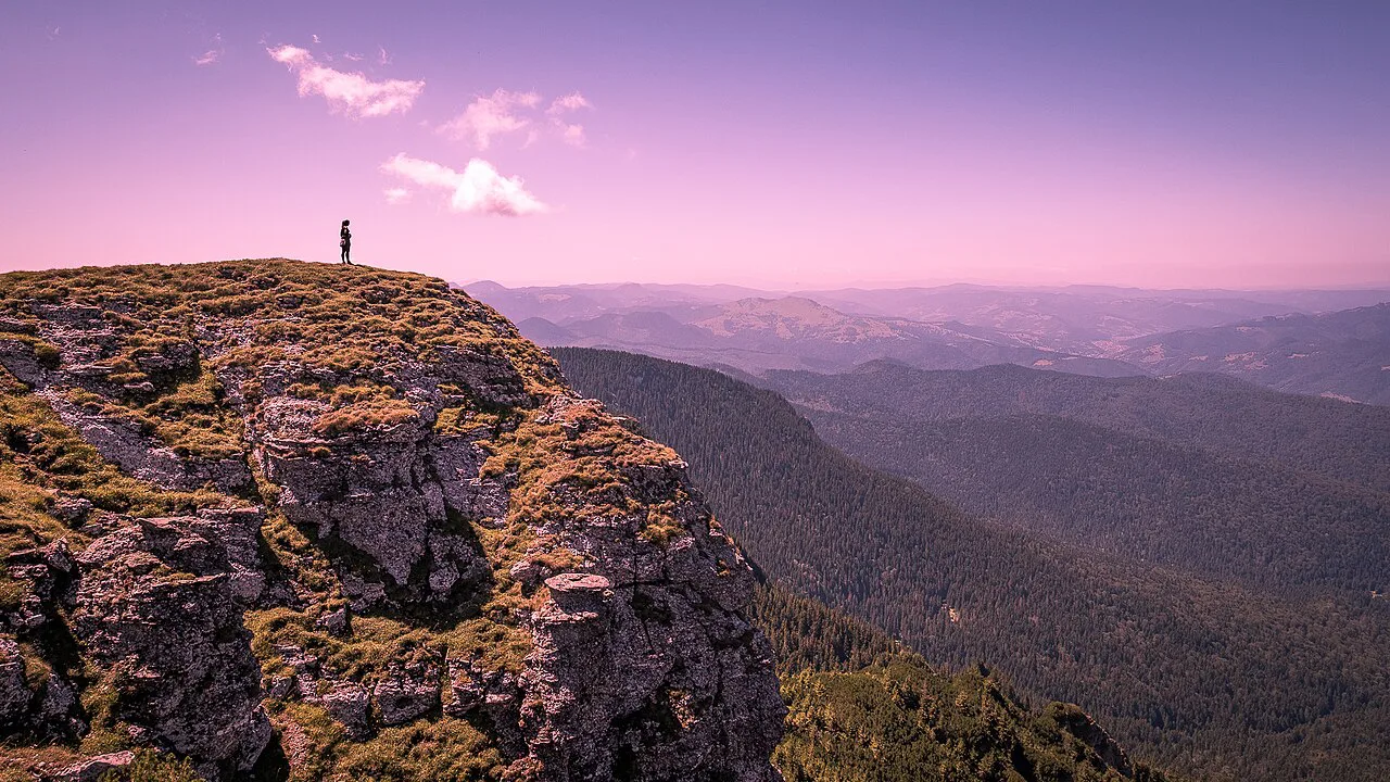 Hiker on a rocky outcrop of the Ceahlău Massif at dusk.